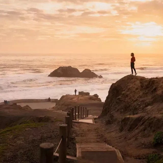 Dos personas están de pie sobre rocas con vistas al océano en Sutro Baths en San Francisco.